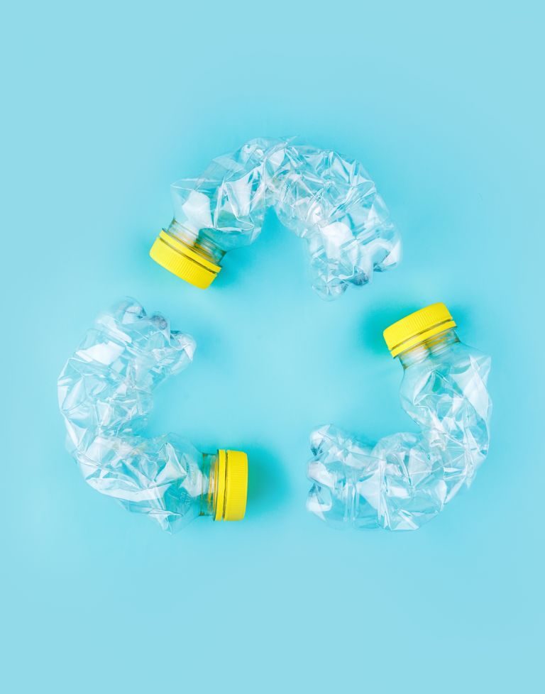 Drei zerdrückte Plastikflaschen mit gelben Deckeln bilden auf hellblauem Hintergrund ein Recycling-Symbol.